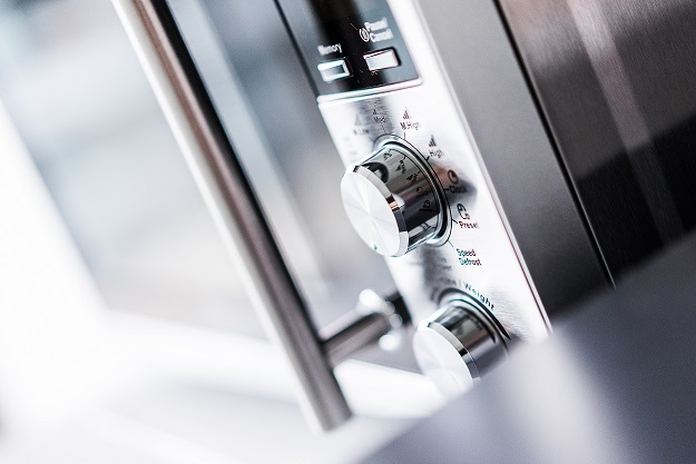 Close-up of a stainless steel microwave's control panel, dial and door handle